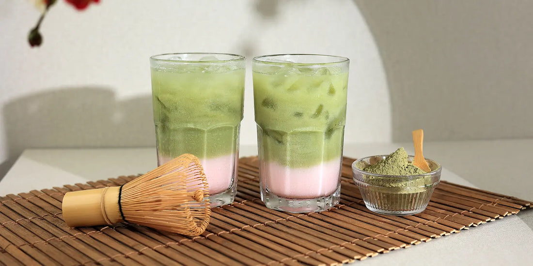 Iced Matcha Latte mit Erdbeerpüree-Schicht, Bambusbesen und Matcha-Pulver im Glas