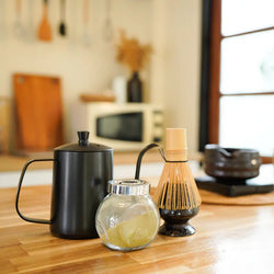 Wasserkocher mit Bambusbesen und Matcha-Schale auf Holztisch für traditionelle japanische Zubereitung