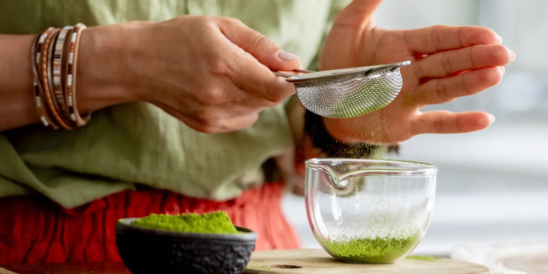 Matcha-Pulver wird durch feines Teesieb in Glas gesiebt zur klumpenfreien Zubereitung