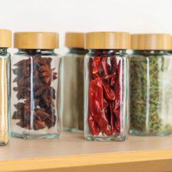 Bio-Gewürze in Glasgläsern mit Bambusdeckeln auf Holzregal – Sternanis, Chili und getrocknete Kräuter
